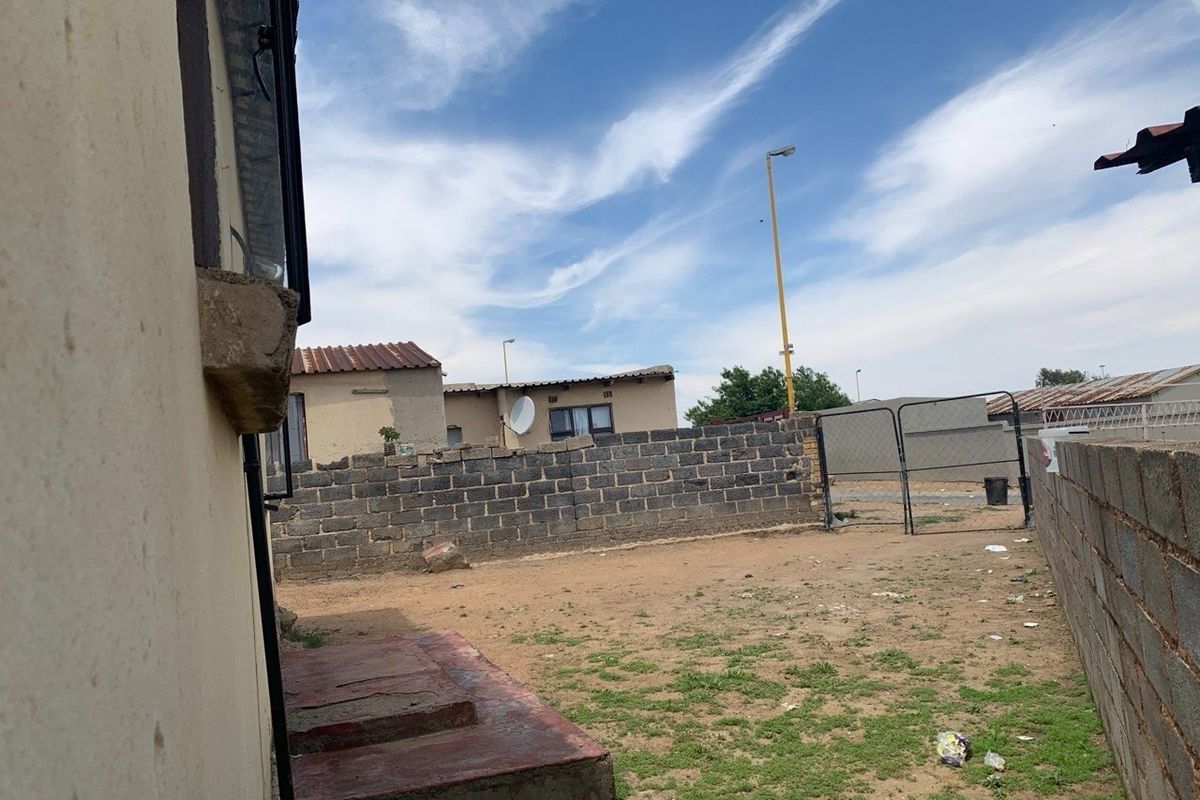 A rear exterior view of the property featuring a concrete block boundary wall, metal gate, and a concrete step leading to the house.