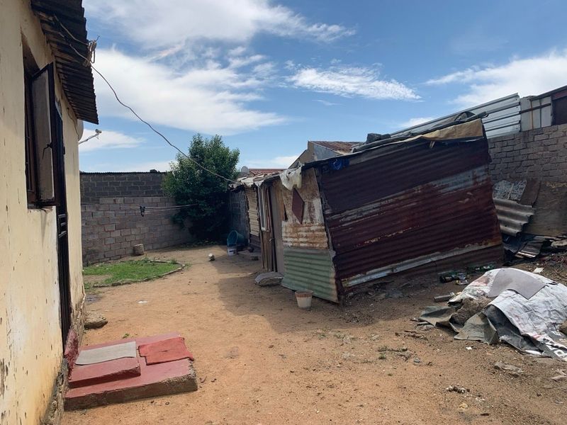 Rear yard area featuring a corrugated iron structure, brick boundary walls, and unpaved ground.
