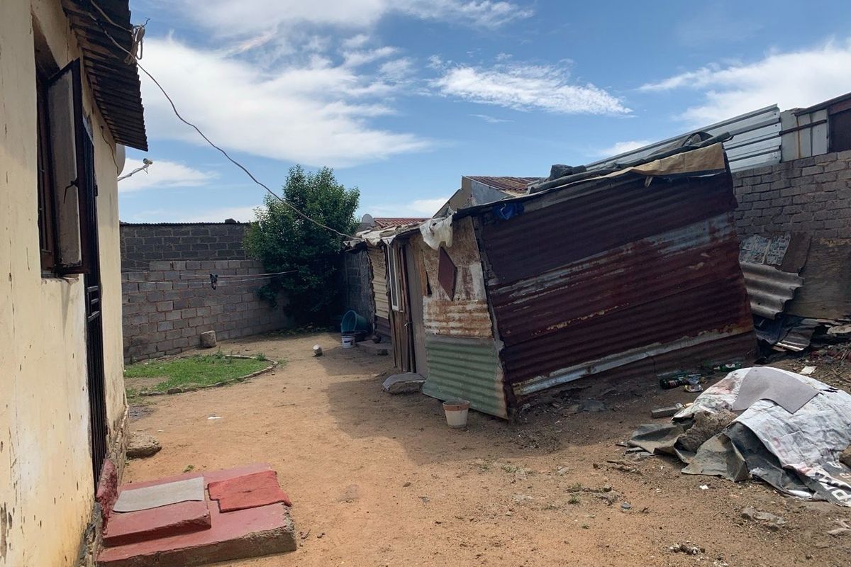 Rear yard area featuring a corrugated iron structure, brick boundary walls, and unpaved ground.