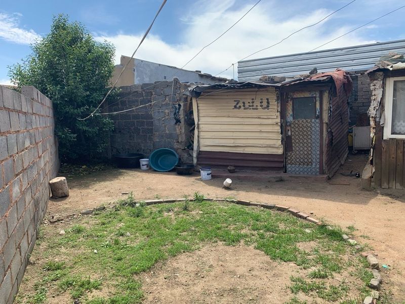 Rear yard area featuring a concrete block boundary wall and a small, weathered corrugated metal structure requiring significant maintenance or replacement.