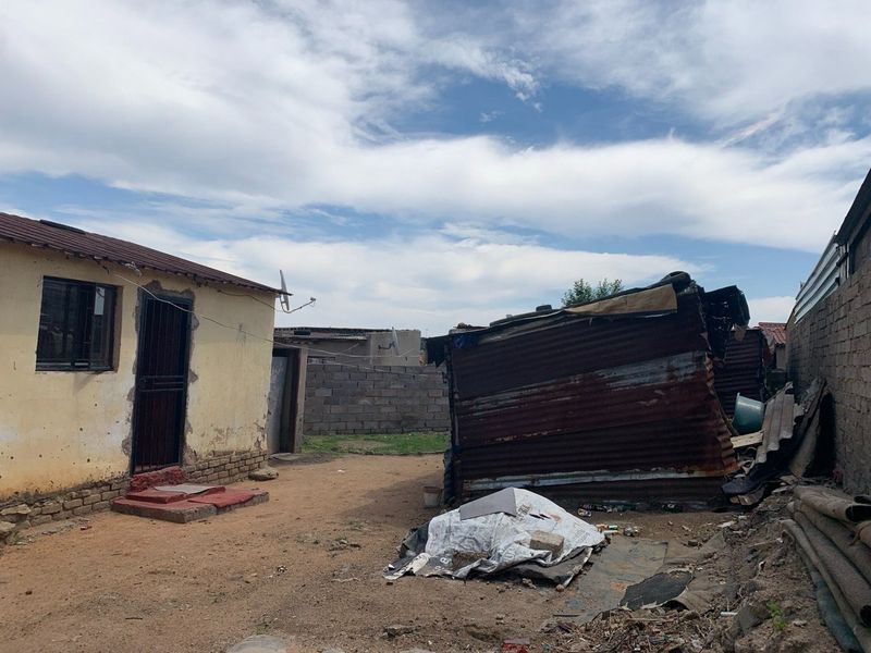 Rear yard area featuring a main dwelling with security gate and a secondary corrugated iron outbuilding structure in need of significant maintenance.