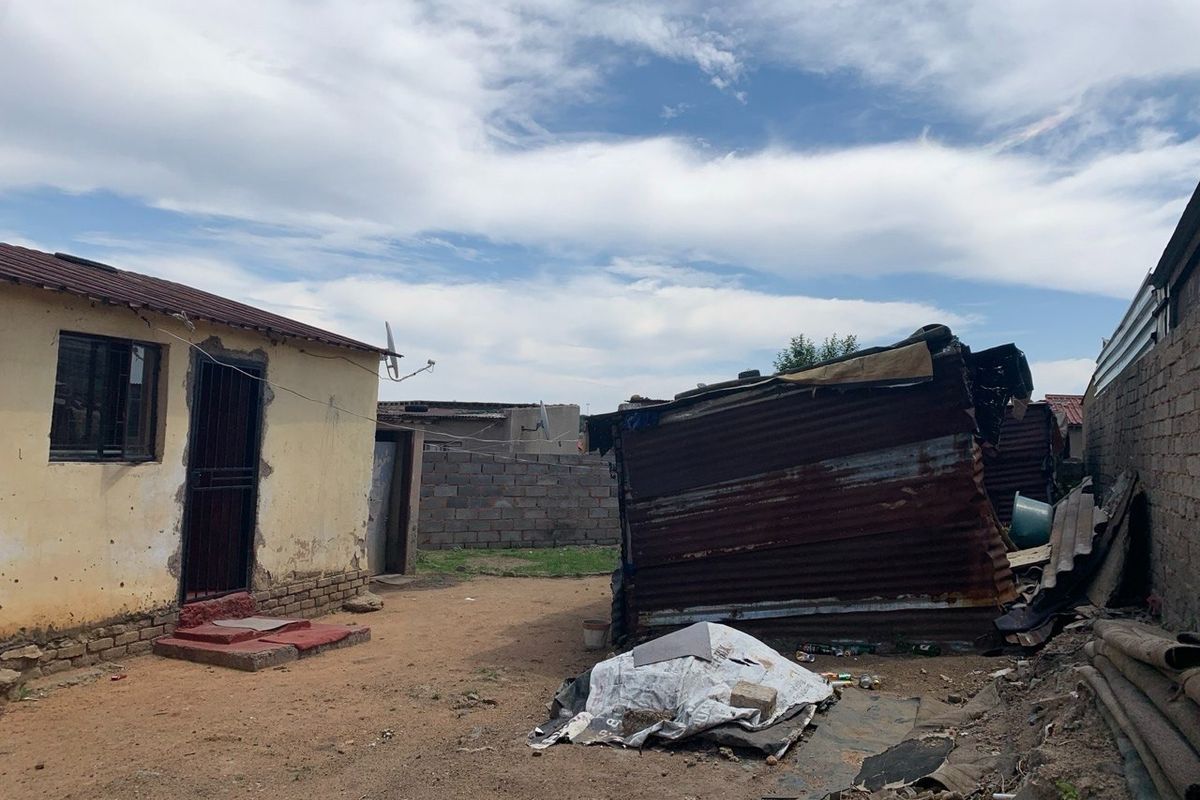 Rear yard area featuring a main dwelling with security gate and a secondary corrugated iron outbuilding structure in need of significant maintenance.