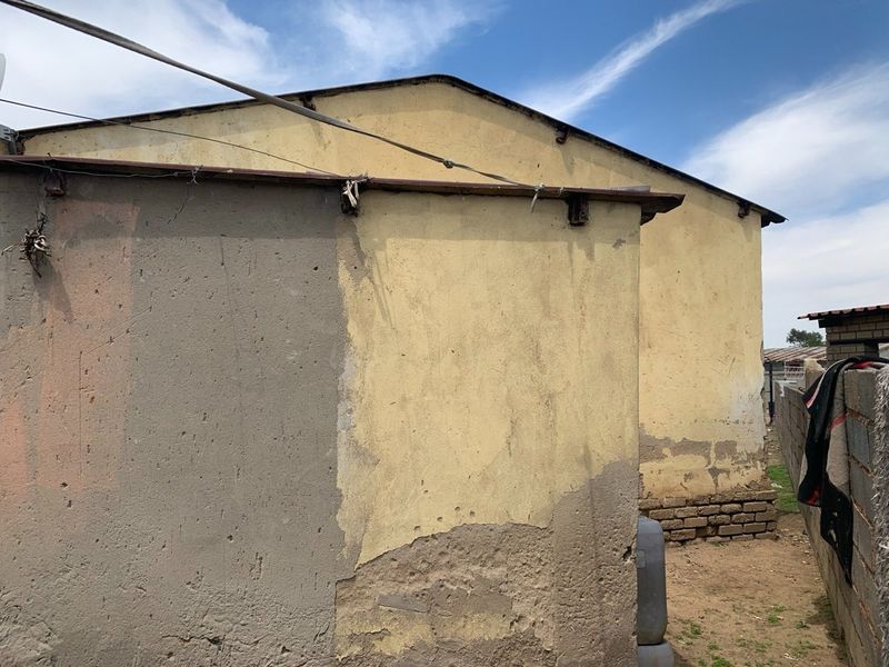 Rear view of the property showing plastered masonry walls with visible signs of wear, peeling paint, and exposed brickwork sections.