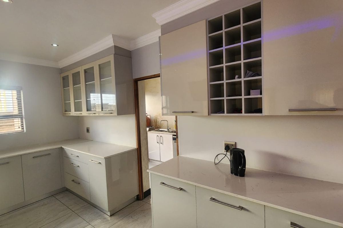Modern kitchen featuring high-gloss cabinetry, stone countertops, integrated wine storage, and glass-fronted display cabinets, leading into a functional scullery area.
