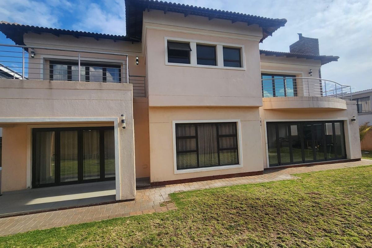A well-maintained double-story rear elevation featuring a paved patio, upper-level balconies with stainless steel balustrades, and large sliding doors opening onto a garden.
