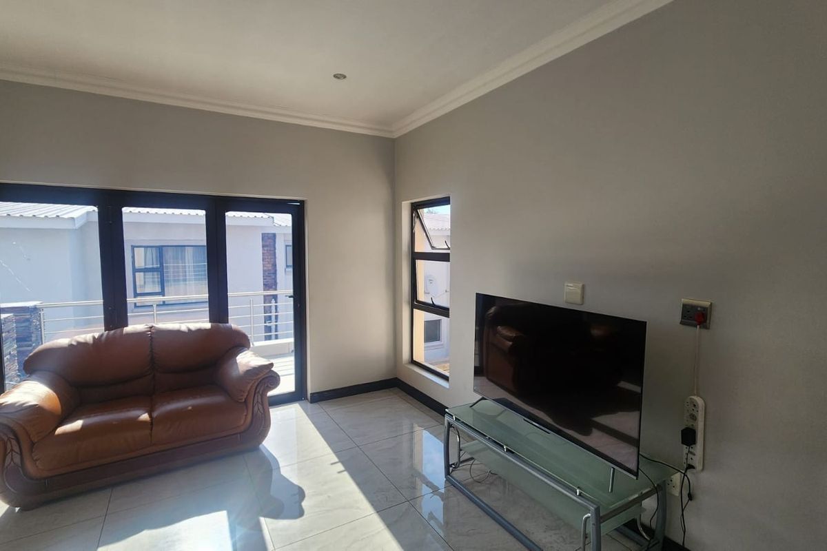 A bright living room featuring large aluminium sliding doors leading to a balcony, tiled flooring, and neutral wall finishes.