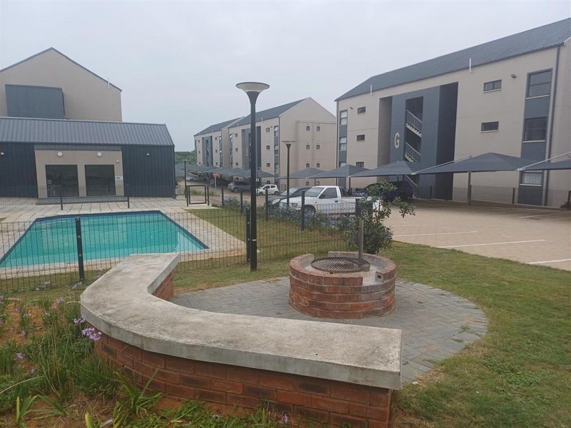 Communal outdoor area featuring a swimming pool, brick built-in braai, concrete seating, and paved patio space within a residential apartment complex.