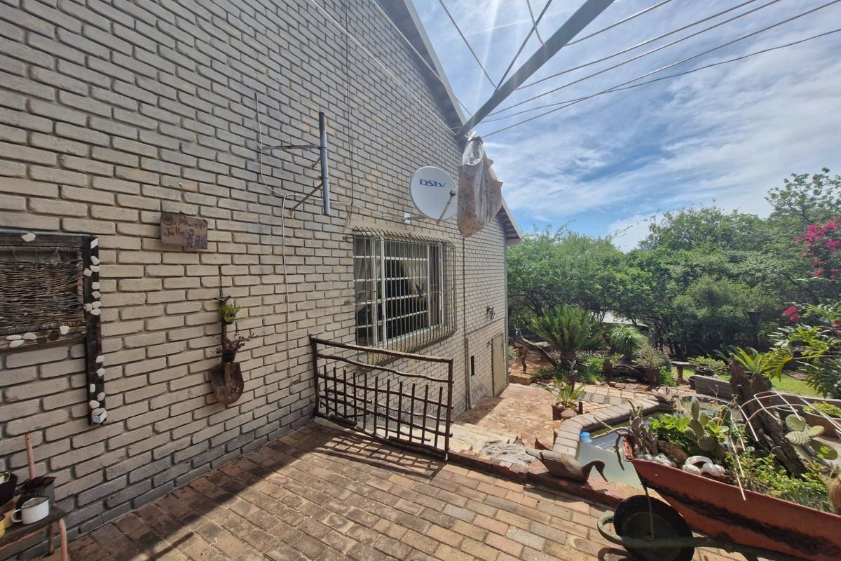 A rear exterior view of the property featuring a brick facade, security bars on windows, and a paved patio area overlooking the garden.