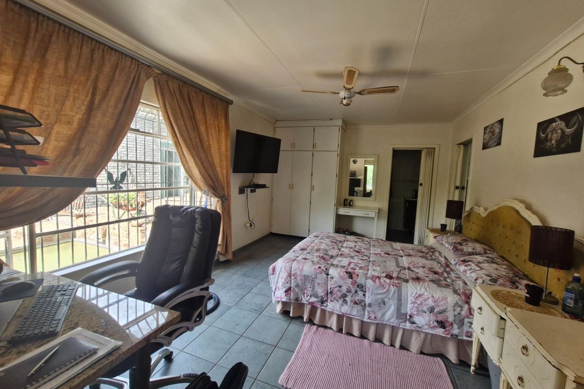 Spacious bedroom featuring tiled flooring, built-in cupboards, a ceiling fan, and large windows with security bars, offering a functional and comfortable living space.