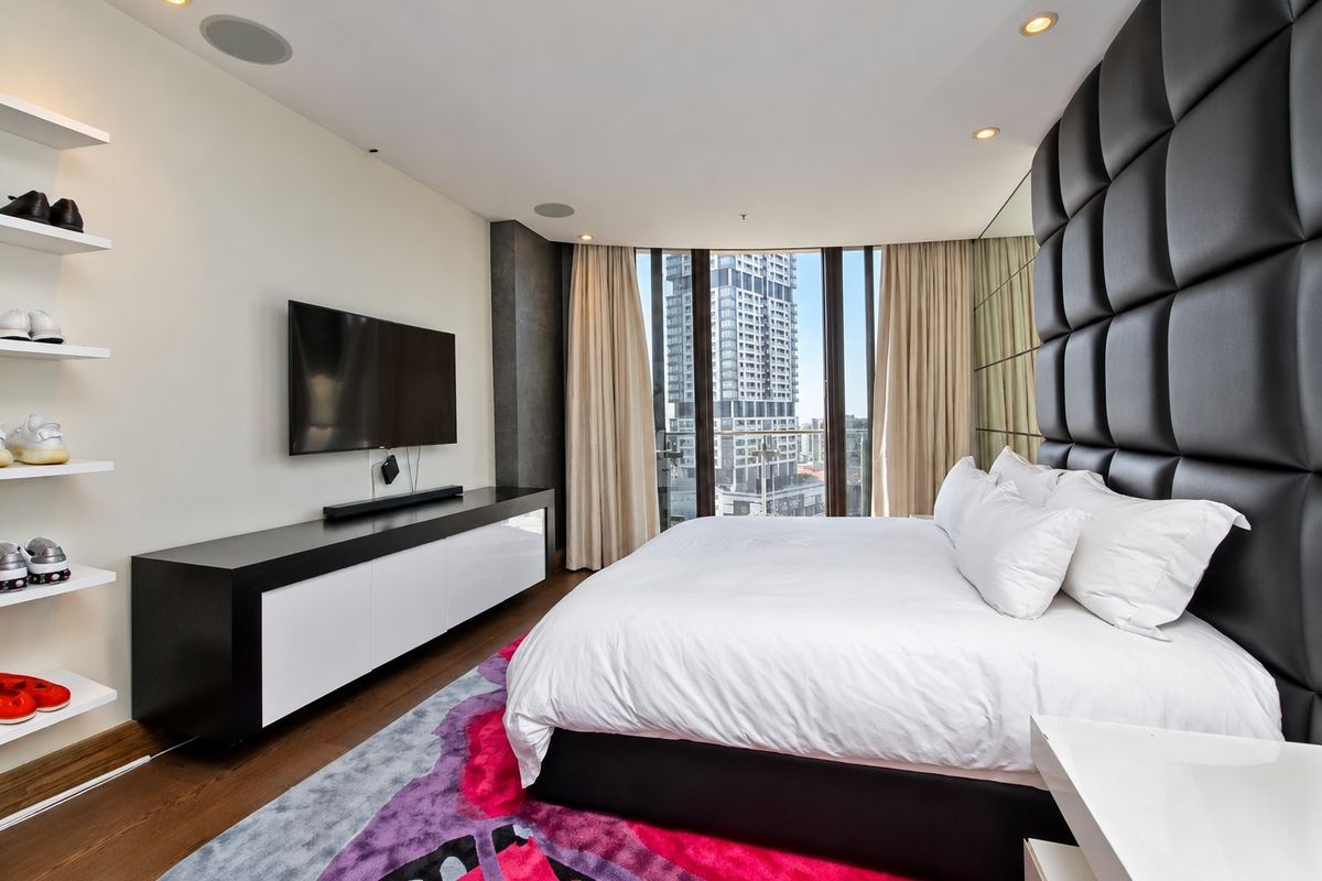 Modern bedroom featuring hardwood floors, floor-to-ceiling windows with city views, recessed lighting, integrated ceiling speakers, and a stylish mirrored feature wall.