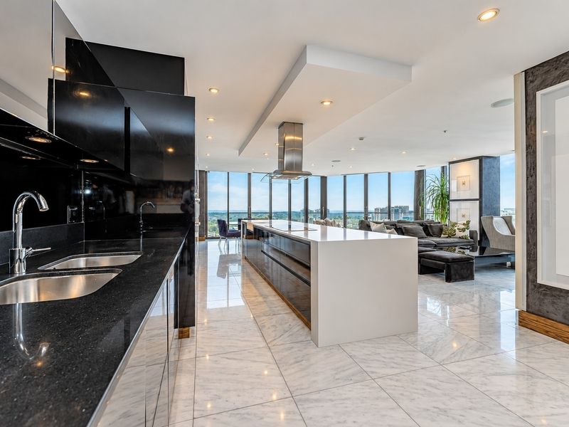 Modern open-plan kitchen and living area featuring a large island, sleek black cabinetry, marble flooring, and expansive floor-to-ceiling windows with panoramic views.