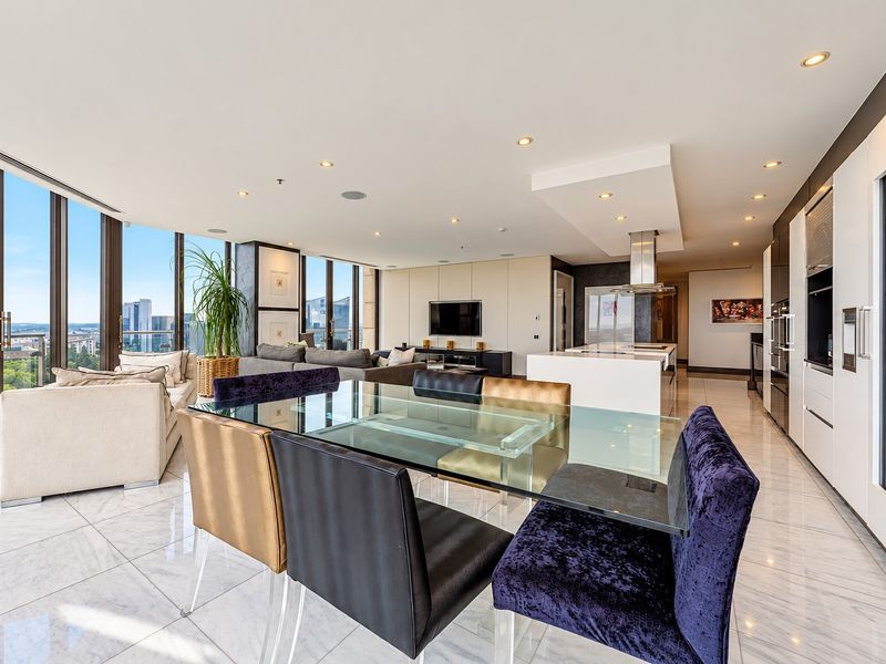 Spacious open-plan living, dining, and kitchen area featuring marble flooring, floor-to-ceiling windows with city views, and modern integrated kitchen appliances.