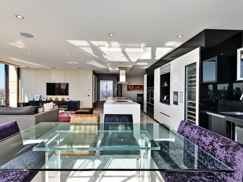 A modern open-plan living and kitchen area featuring high-end built-in appliances, sleek cabinetry, and expansive windows with city views.