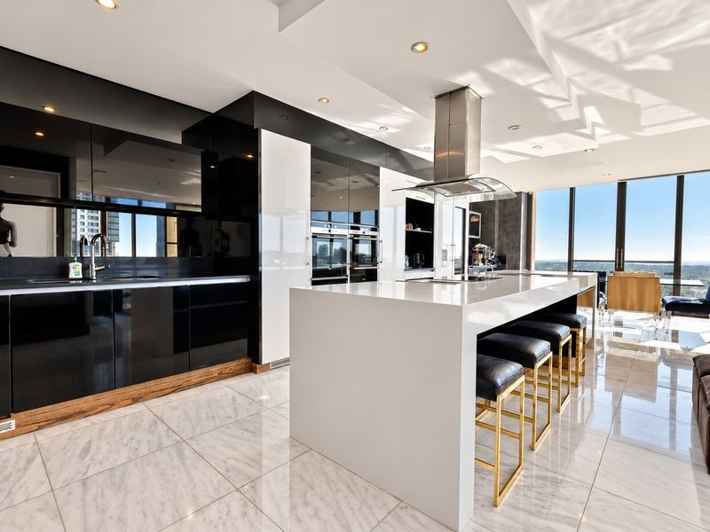 Modern high-end kitchen featuring a large central island, sleek high-gloss cabinetry, built-in appliances, and polished marble flooring with expansive city views.