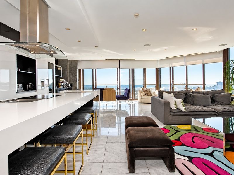 Modern open-plan living area featuring a sleek kitchen with stone island, high-end appliances, marble flooring, and expansive floor-to-ceiling windows with panoramic views.