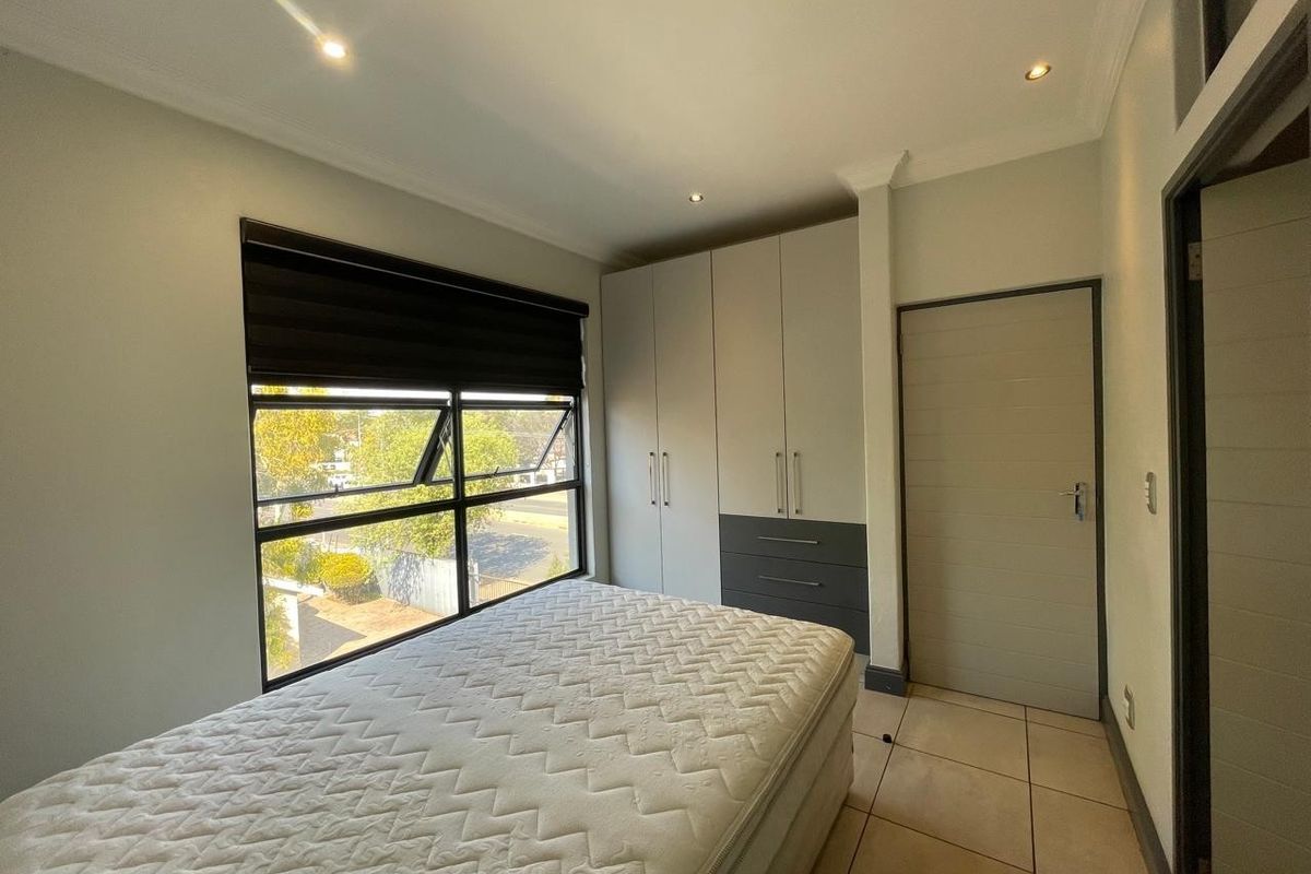 A well-maintained bedroom featuring built-in cupboards, tiled flooring, recessed downlighting, and a large window with a roller blind.