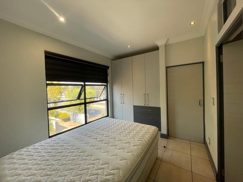A well-maintained bedroom featuring built-in cupboards, tiled flooring, recessed downlighting, and a large window with a roller blind.