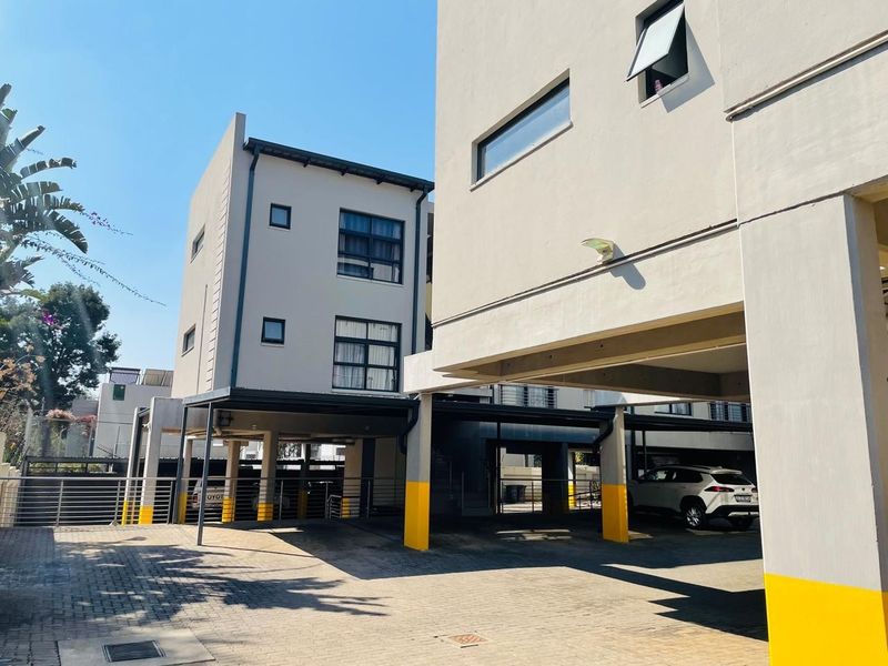Exterior view of the apartment complex featuring a paved driveway and covered parking bays with concrete support structures.