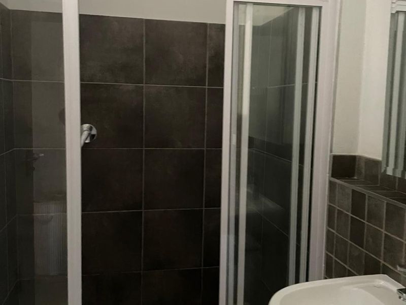A functional bathroom featuring a shower enclosure with dark tiled walls and a pedestal basin with a tiled splashback.