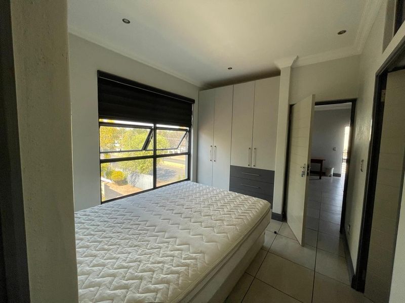 A well-maintained bedroom featuring built-in cupboards, tiled flooring, and large aluminium windows that provide ample natural light.