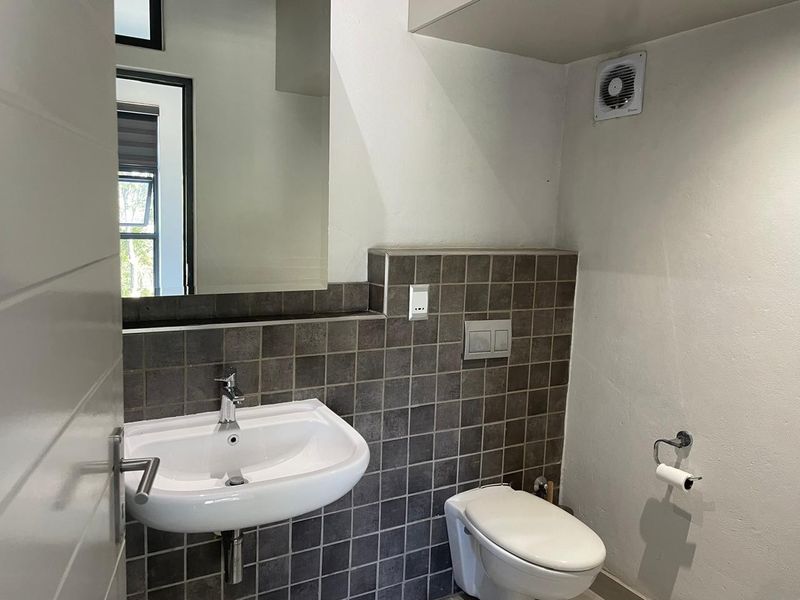 A clean, modern bathroom featuring a wall-mounted basin, wall-hung toilet with concealed cistern, and dark tiled splashback.