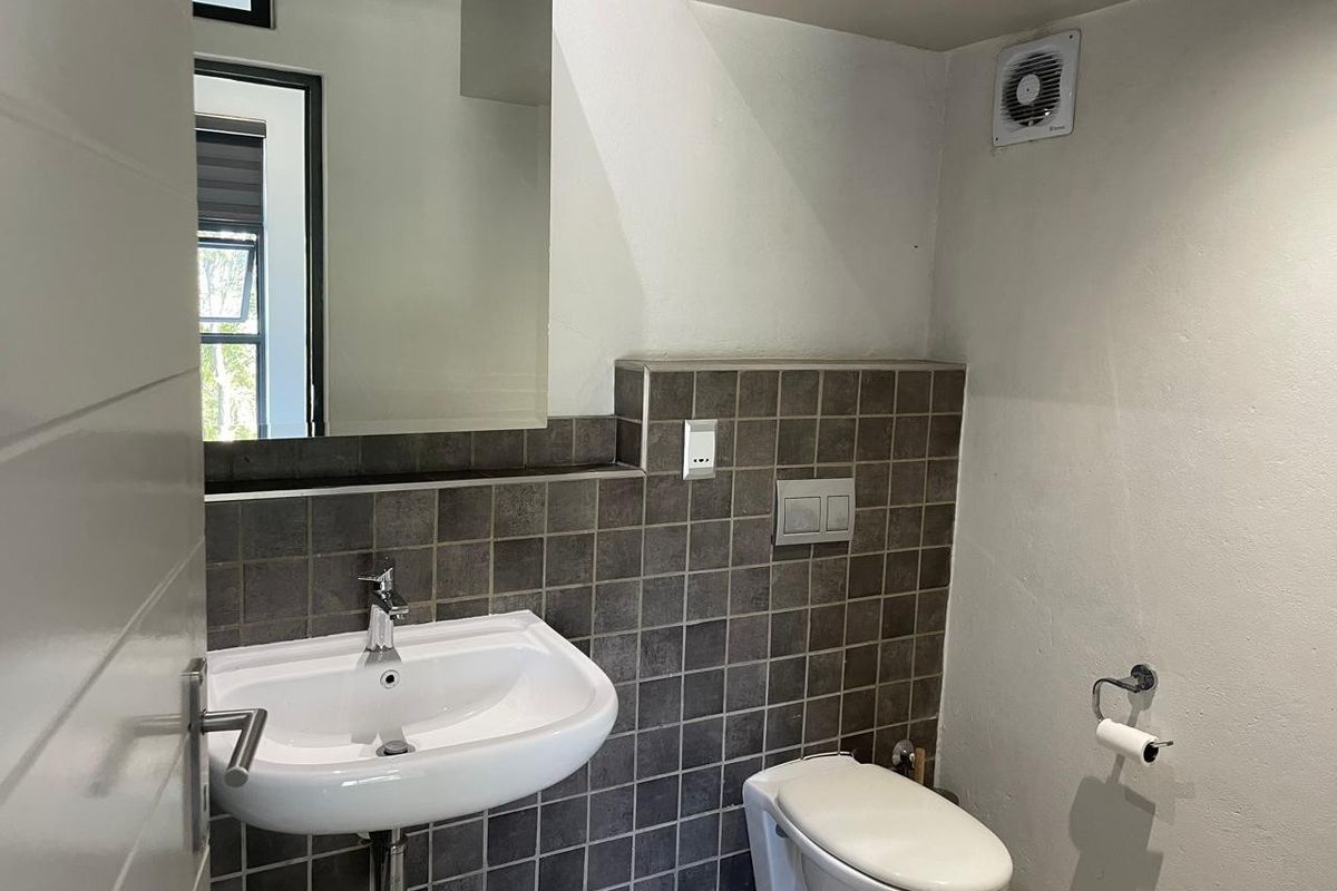 A clean, modern bathroom featuring a wall-mounted basin, wall-hung toilet with concealed cistern, and dark tiled splashback.
