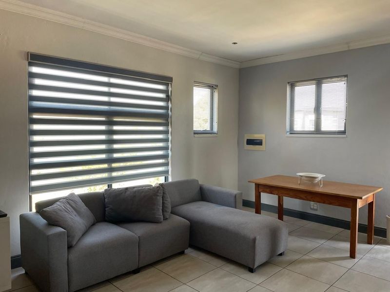 A bright living area featuring neutral tiled flooring, modern zebra blinds, and clean wall finishes, providing a versatile space for relaxation or dining.