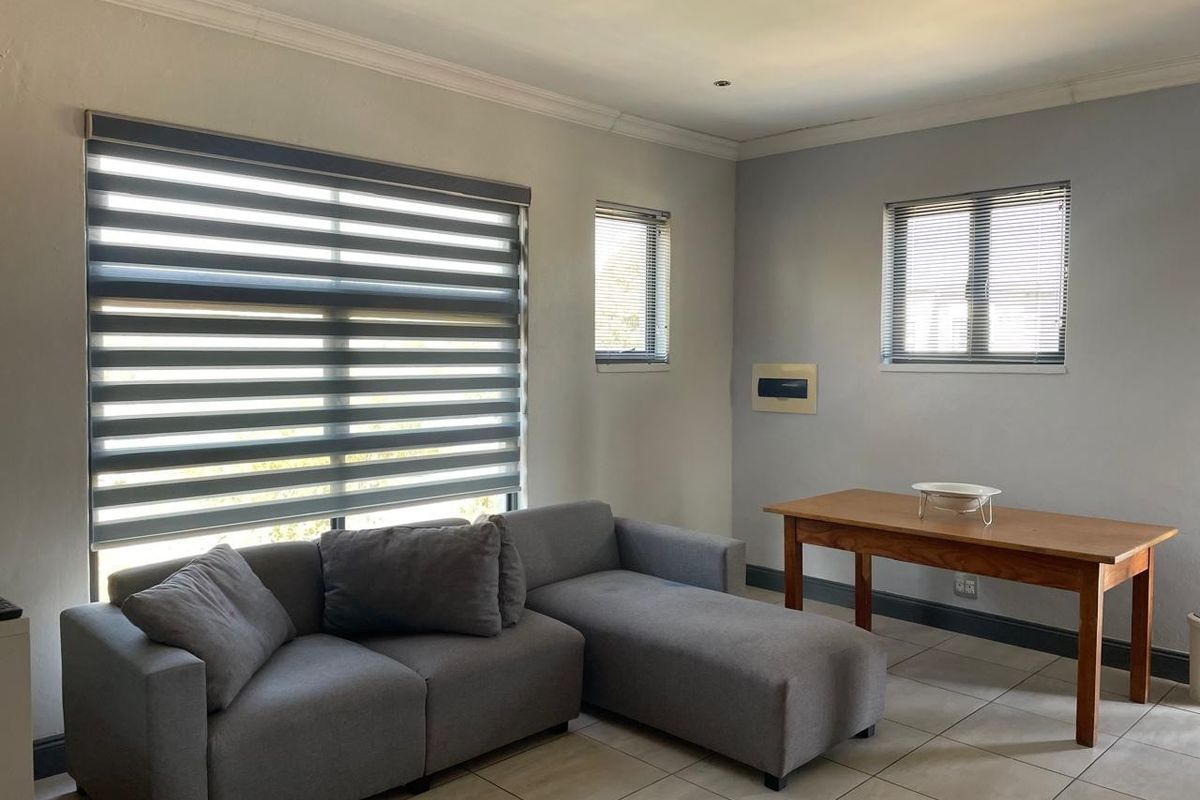 A bright living area featuring neutral tiled flooring, modern zebra blinds, and clean wall finishes, providing a versatile space for relaxation or dining.