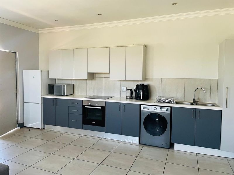 Modern kitchen featuring two-tone cabinetry, integrated oven and hob, tiled splashback, and tiled flooring in an open-plan layout.