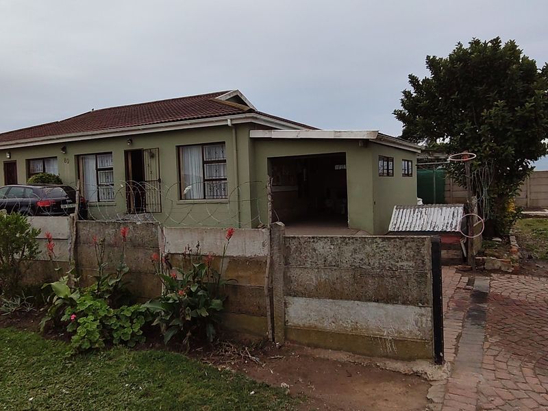 Front elevation of a single-story house featuring a tiled roof, attached carport, and a concrete boundary wall with security fencing.