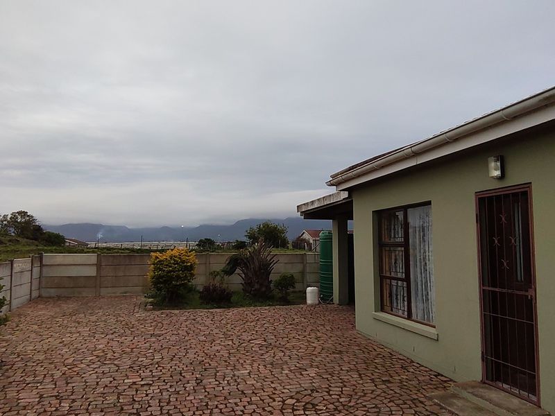 Rear exterior view of the property featuring a paved courtyard, precast boundary wall, and a water tank with mountain views in the distance.