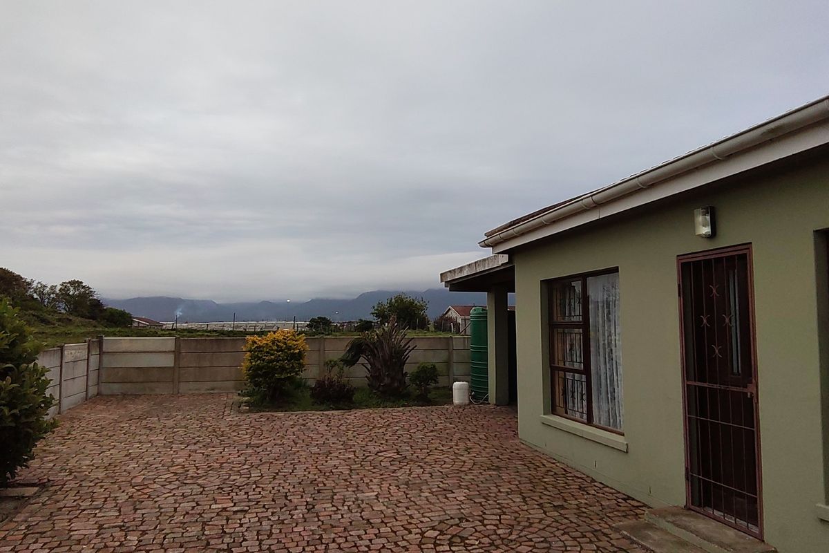 Rear exterior view of the property featuring a paved courtyard, precast boundary wall, and a water tank with mountain views in the distance.