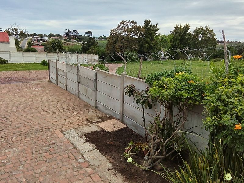 Rear exterior area featuring a precast concrete boundary wall with razor wire security and a brick paved driveway.