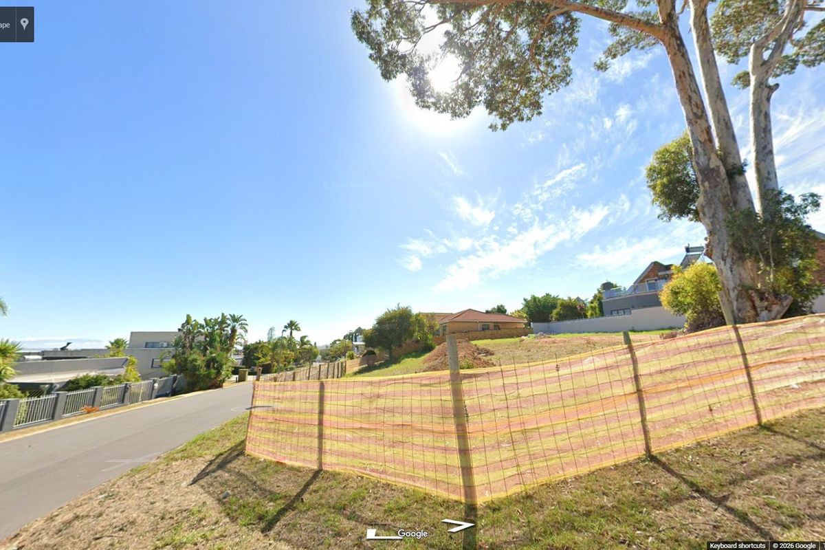 A street-level view of a vacant residential plot featuring perimeter fencing and established trees in a suburban neighborhood.