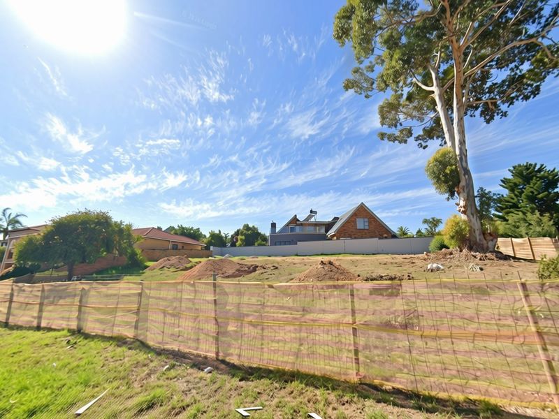 A vacant residential plot featuring perimeter fencing, mature trees, and uneven ground with soil mounds, ready for development.