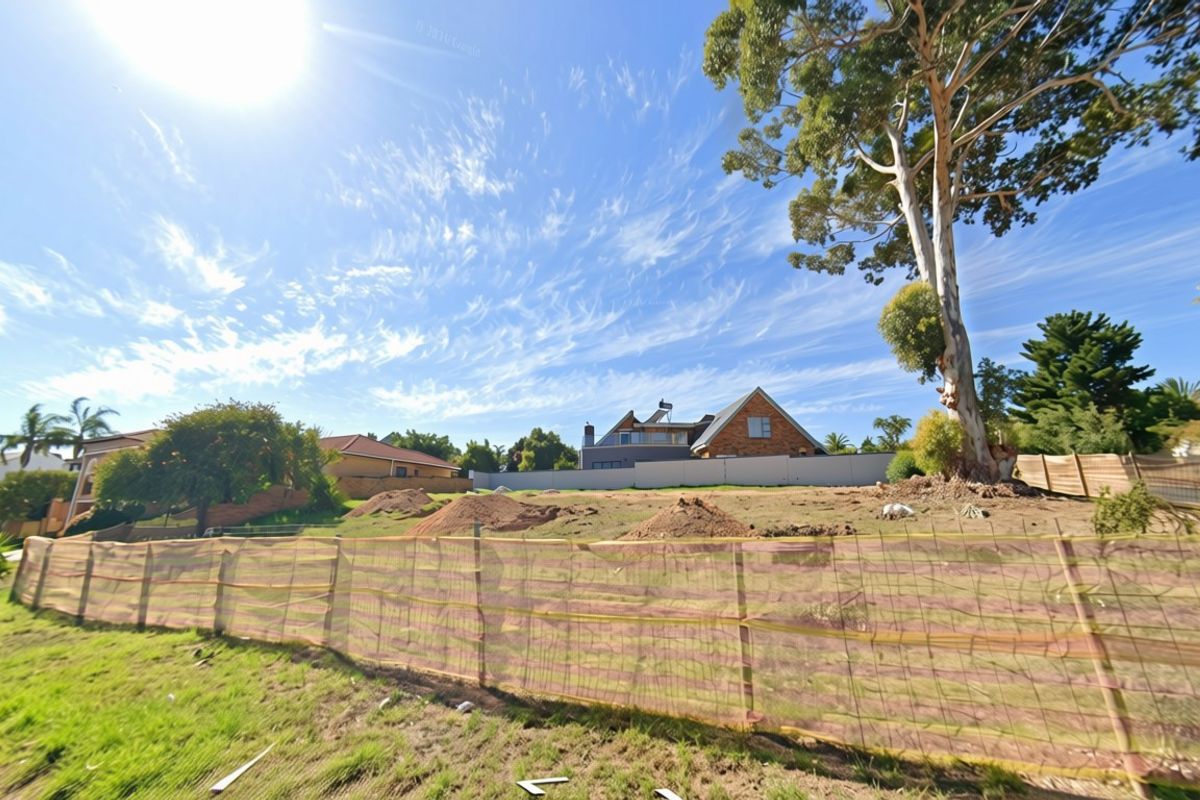 A vacant residential plot featuring perimeter fencing, mature trees, and uneven ground with soil mounds, ready for development.