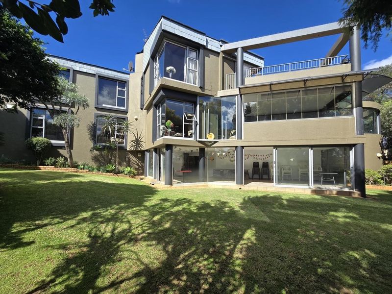Rear view of a modern multi-story house featuring extensive glass facades, a spacious lawn, and a balcony with metal railings.