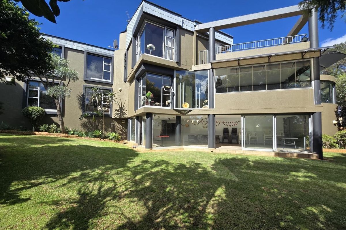 Rear view of a modern multi-story house featuring extensive glass facades, a spacious lawn, and a balcony with metal railings.
