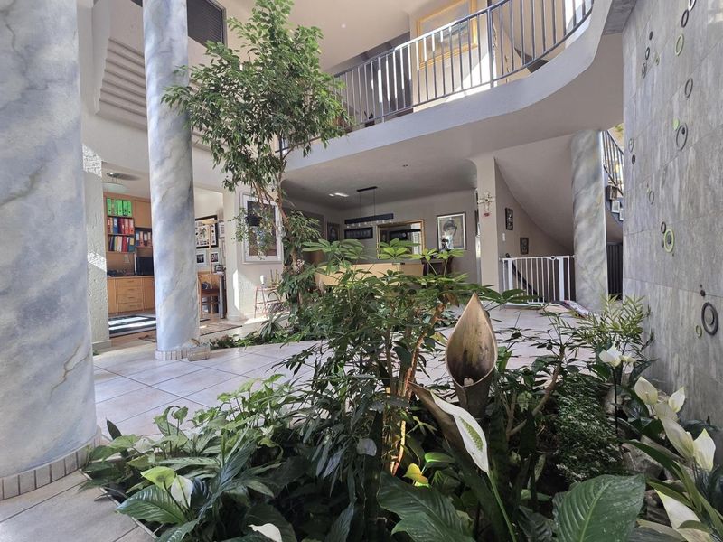 Spacious double-volume entrance hall featuring an indoor garden, marble-effect columns, and a mezzanine balcony with a wrought iron balustrade.