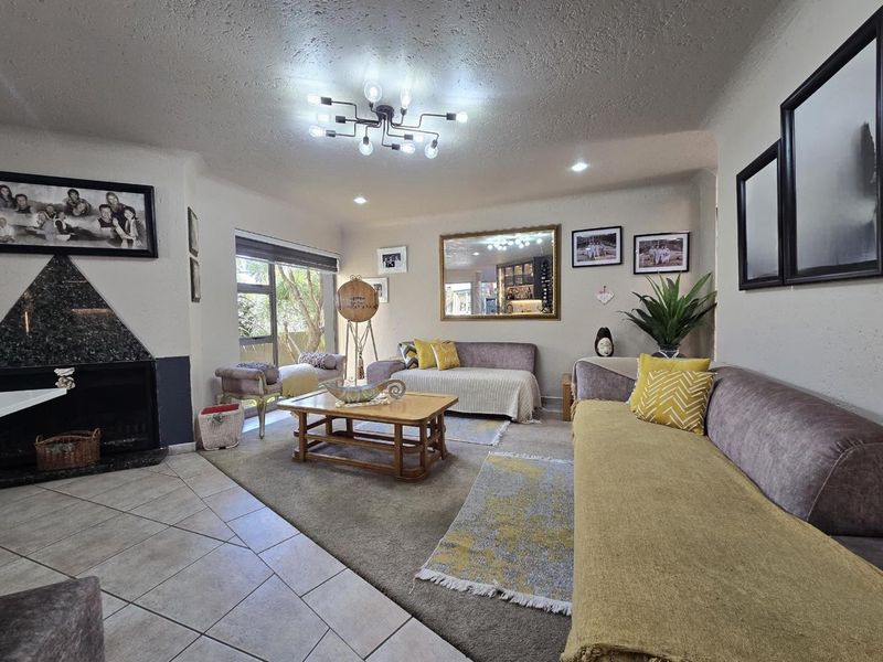 A comfortable living room featuring a striking granite-surround fireplace, a mix of tiled and carpeted flooring, and modern overhead lighting.