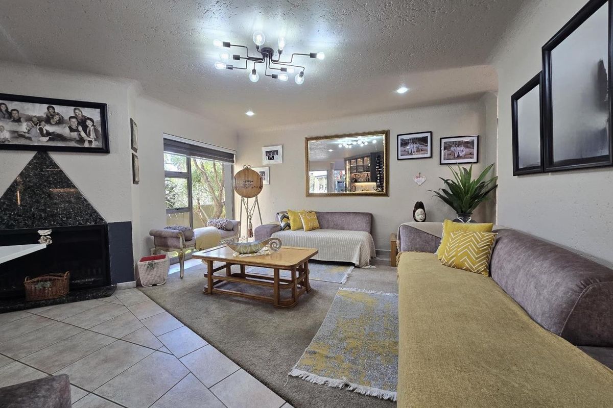 A comfortable living room featuring a striking granite-surround fireplace, a mix of tiled and carpeted flooring, and modern overhead lighting.