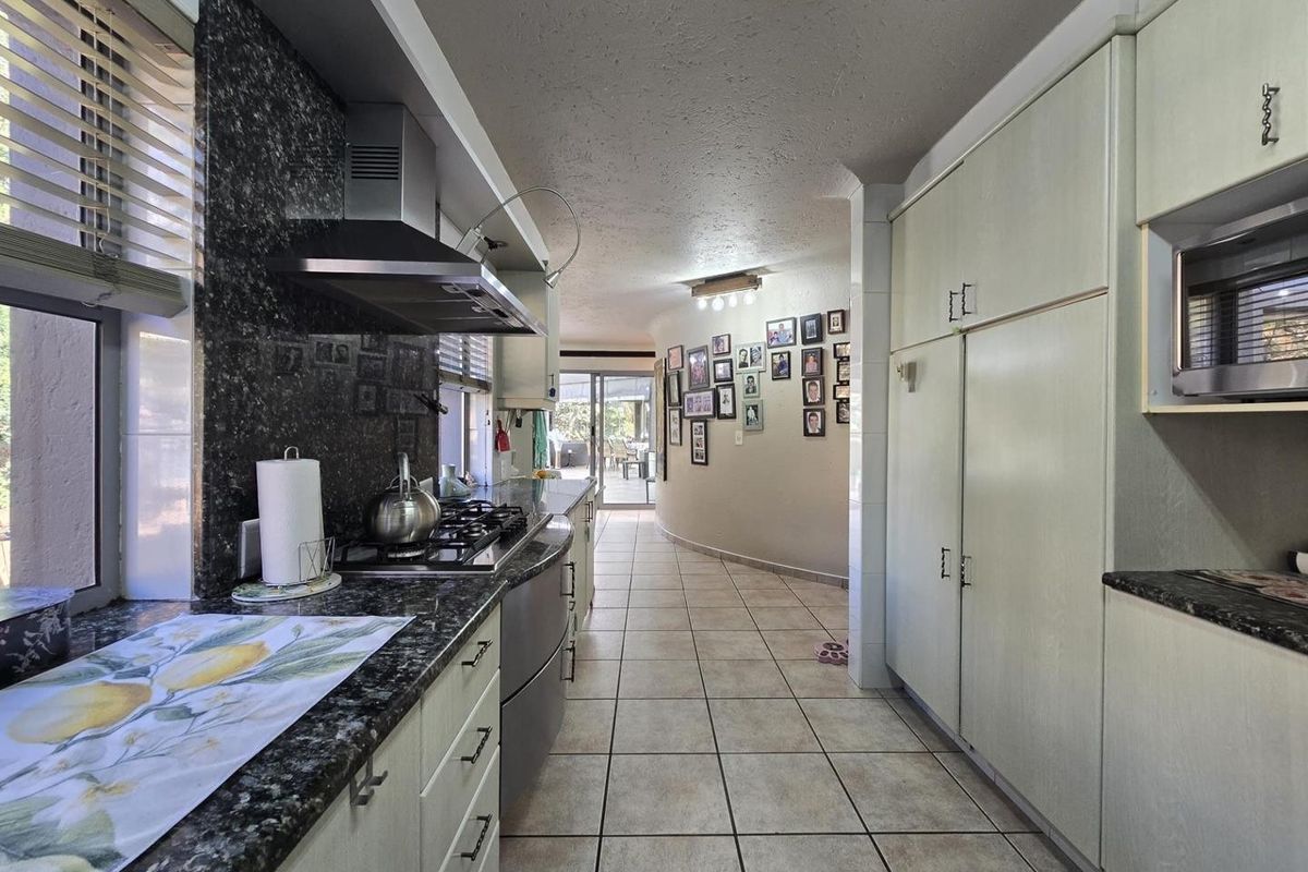 A functional kitchen featuring granite countertops, a gas hob with extractor fan, built-in cabinetry, and tiled flooring, leading towards an open living area.