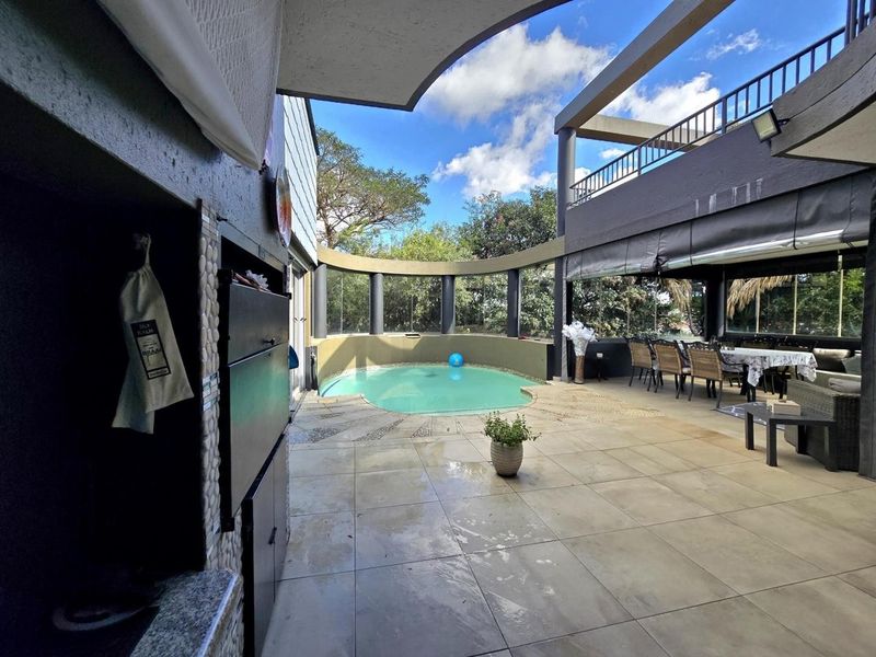 Spacious outdoor entertainment area featuring a swimming pool, covered patio, and built-in braai, perfect for hosting and relaxation.