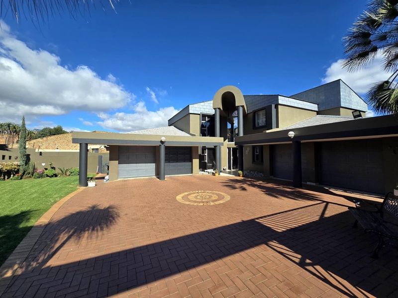 A well-maintained modern house exterior featuring a spacious paved driveway, multiple garage bays, and a distinctive covered entrance with architectural columns.