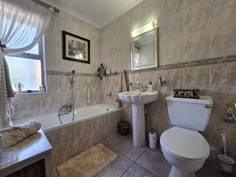 A functional bathroom featuring a pedestal basin, bathtub with shower mixer, and toilet, finished with neutral wall and floor tiling.