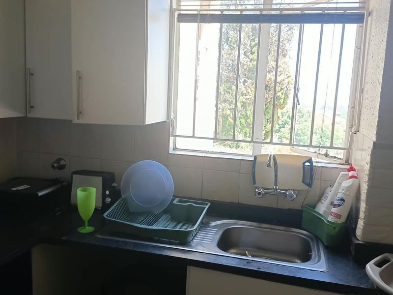 A functional kitchen area featuring a stainless steel sink, tiled splashback, and built-in cabinetry with a window providing natural light.