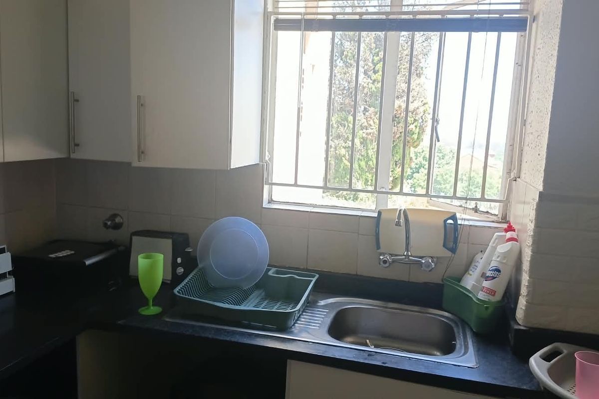 A functional kitchen area featuring a stainless steel sink, tiled splashback, and built-in cabinetry with a window providing natural light.