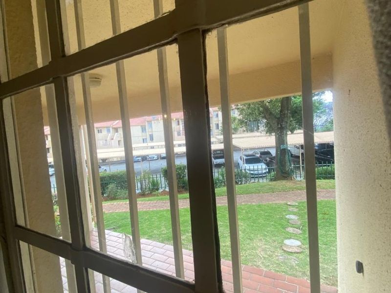 View from inside looking out through security bars onto a paved patio, garden area, and communal parking space.