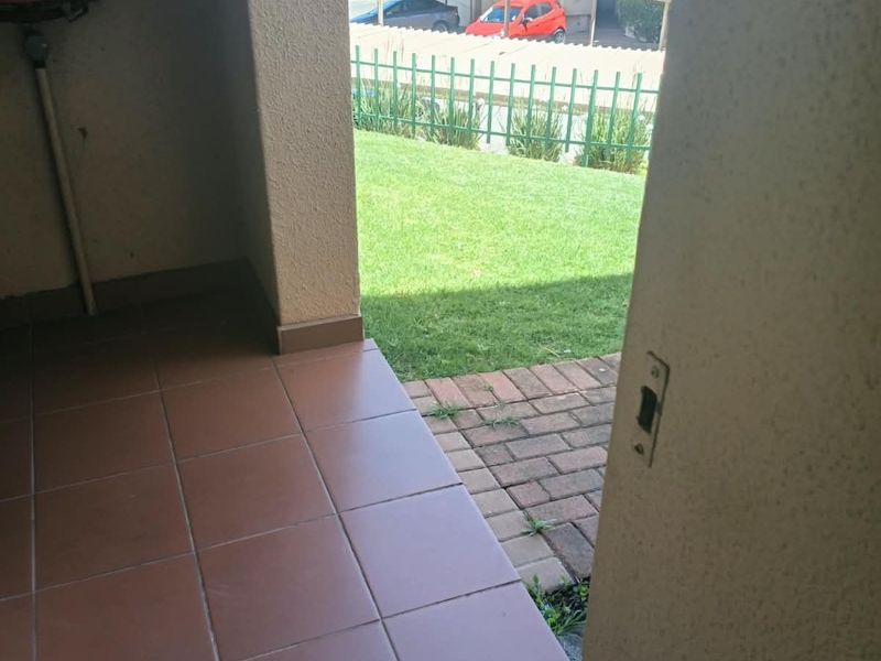 A covered patio area featuring tiled flooring, a wall-mounted fire hose reel, and direct access to a small paved and lawned garden space.