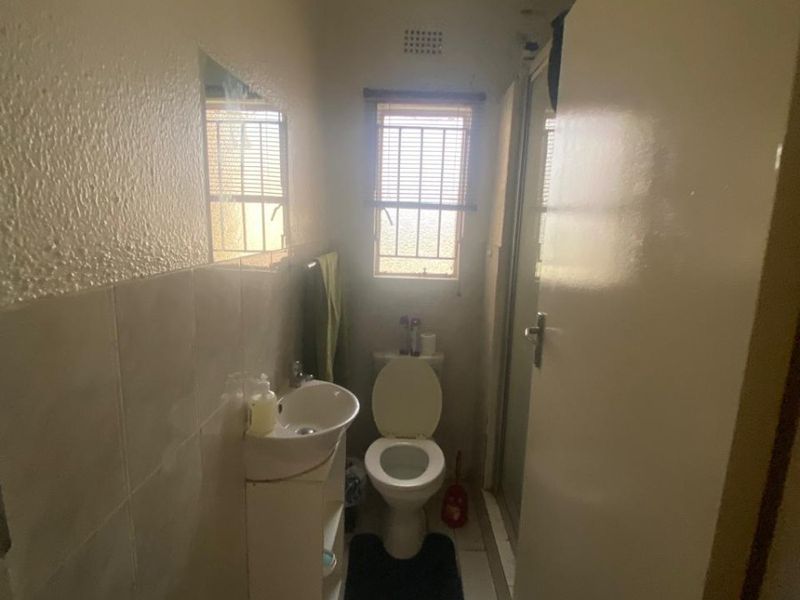 A compact bathroom featuring a pedestal basin, toilet, and shower enclosure with tiled flooring and wall finishes.